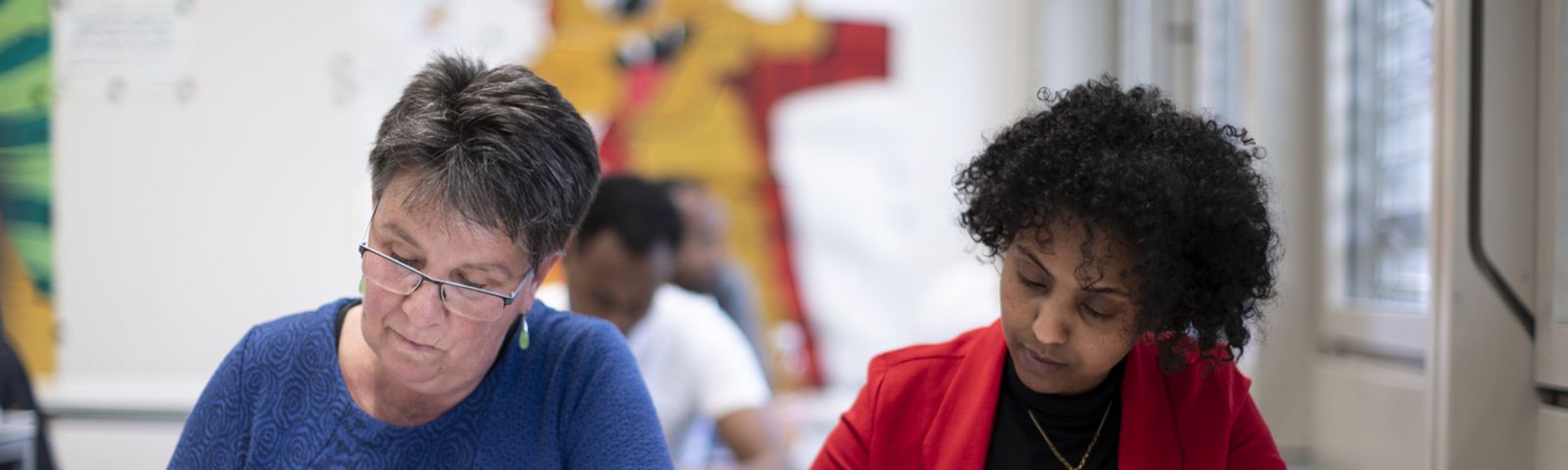 Zwei geflüchtete Frauen schreiben einen Text in einem Schulzimmer.