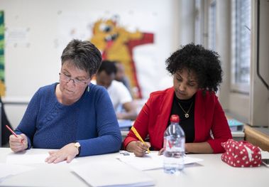 Zwei geflüchtete Frauen schreiben einen Text in einem Schulzimmer.